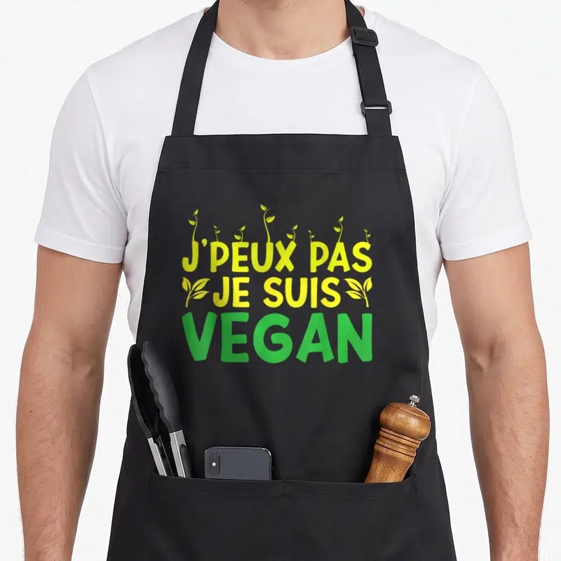 Tablier de cuisine noir avec inscription j'peux pas je suis vegan en jaune et vert entourée de jeunes pousses.