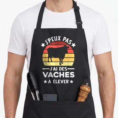 Tablier de cuisine noir avec motif rétro représentant une vache et le texte J'peux pas j'ai des vaches à élever.