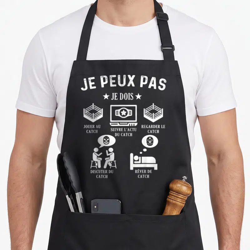 Tablier de cuisine noir avec inscription Je peux pas je dois suivre l'actu du catch et illustrations blanches.