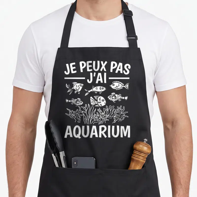 Tablier de cuisine noir avec texte blanc Je peux pas j'ai aquarium et illustrations de poissons stylisés au-dessus de coraux.