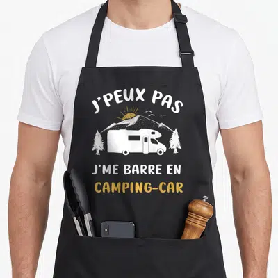 Tablier de cuisine noir avec inscription j'peux pas j'me barre en camping-car et illustration de véhicule blanc sur fond de montagnes.