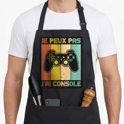 Tablier de cuisine noir avec une manette de jeu vidéo colorée et le texte je peux pas j'ai console imprimé en haut et en bas.
