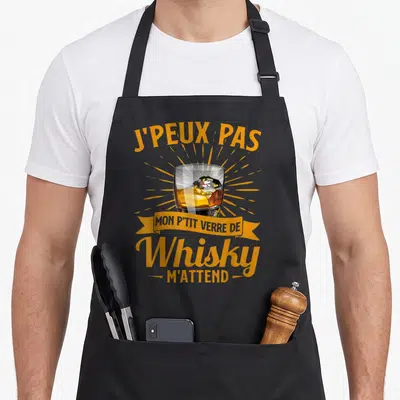 Tablier de cuisine noir avec illustration d'un verre de whisky et texte J'peux pas mon p'tit verre de whisky m'attend en orange.