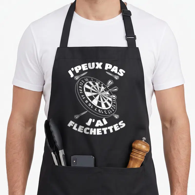 Tablier de cuisine noir avec une cible de fléchettes blanche et l'inscription j'peux pas j'ai fléchettes en lettres capitales.