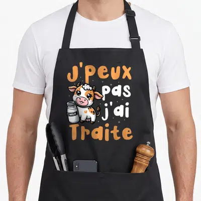 Tablier de cuisine noir avec une vache cartoon tenant un bocal de lait et le texte j'peux pas j'ai traite en orange et blanc.