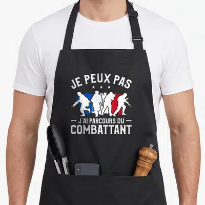 Tablier de cuisine noir avec silhouettes de soldats et texte Je peux pas j'ai parcours du combattant en blanc.