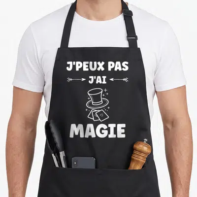 Tablier de cuisine noir avec texte blanc j'peux pas j'ai magie et illustration de chapeau de magicien.
