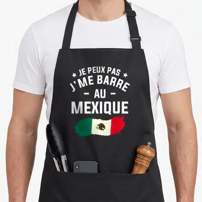 Tablier de cuisine noir avec l'inscription Je peux pas j'me barre au Mexique et un drapeau mexicain stylisé en bas.