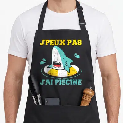 Tablier de cuisine noir avec un requin dans une bouée jaune et le texte j'ai piscine imprimé en bleu.