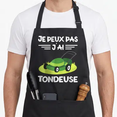 Tablier de cuisine noir avec une tondeuse verte et le texte je peux pas j'ai tondeuse en blanc.