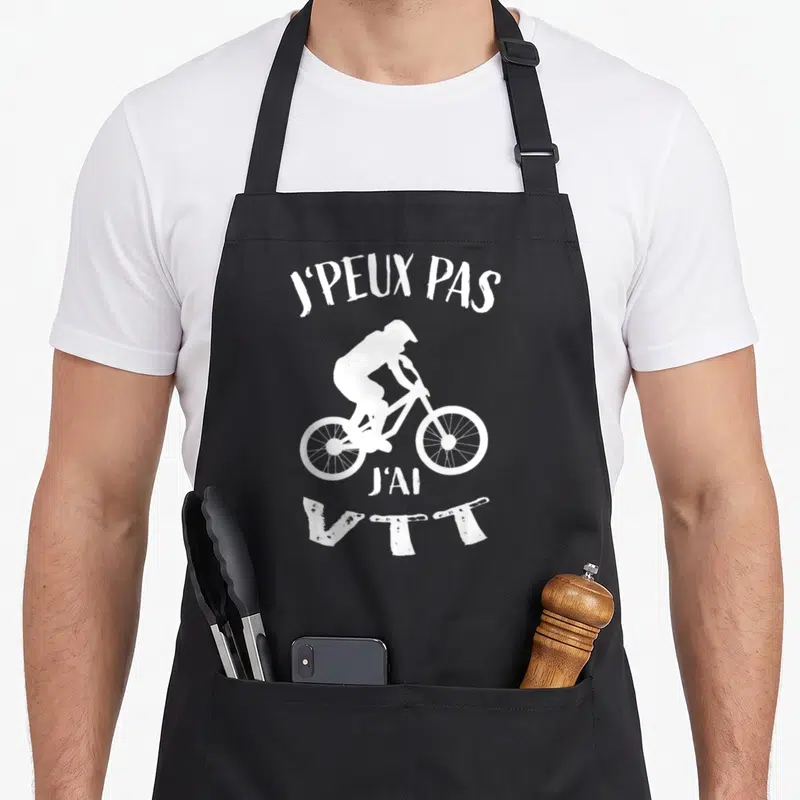 Tablier de cuisine noir avec silhouette blanche de cycliste VTT et texte J'peux pas j'ai VTT imprimé en haut et en bas.