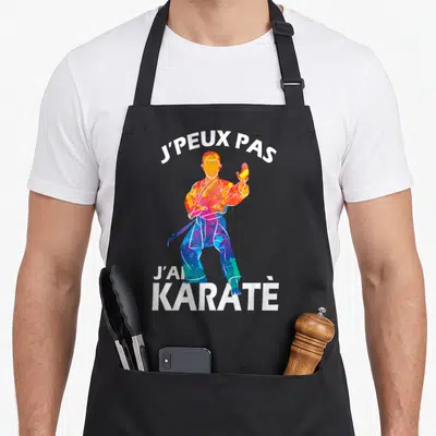 Tablier de cuisine noir avec une silhouette de karatéka multicolore et le texte j'peux pas j'ai karaté en blanc.
