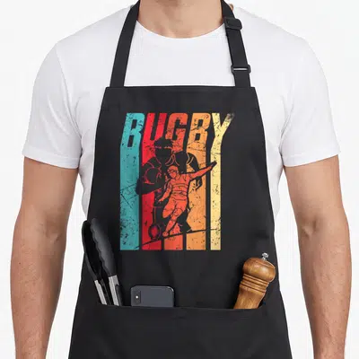 Tablier de cuisine noir avec illustration vintage de joueur de rugby et texte RUGBY multicolore.