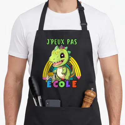 Tablier de cuisine noir avec un dinosaure vert tenant un sac à dos sous l'arc-en-ciel.