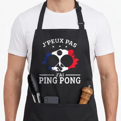 Tablier de cuisine noir avec inscription J'peux pas j'ai Ping Pong et deux paddles croisés sur fond tricolore.