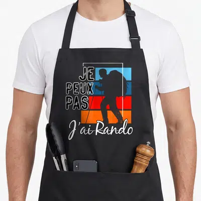 Tablier de cuisine noir avec inscription je peux pas j'ai rando et silhouette de randonneur sur fond de bandes bleues rouges et oranges.