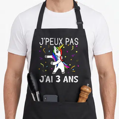 Tablier de cuisine noir avec une licone blanche aux cheveux multicolores effectuant un mouvement de danse sous des confettis.