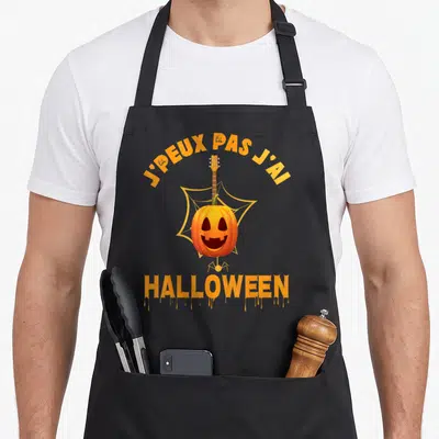 Tablier de cuisine noir avec un pumpkin jouant de la guitare devant une toile d'araignée et le texte J'peux pas j'ai Halloween.