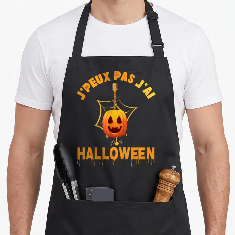 Tablier de cuisine noir avec un pumpkin jouant de la guitare devant une toile d'araignée et le texte J'peux pas j'ai Halloween.