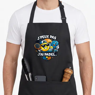 Tablier de cuisine noir avec deux balles de tennis souriantes tenant des raquettes de padel sous un soleil couchant.