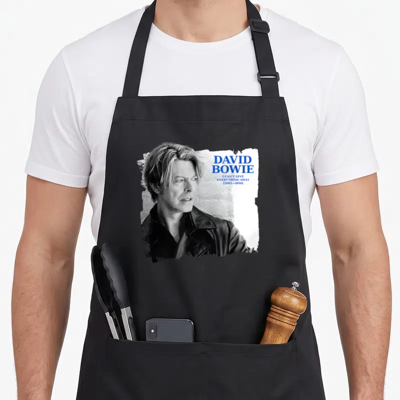 Tablier de cuisine noir avec portrait de David Bowie et texte I can't give everything away 2002-2016 en typographie bleue.