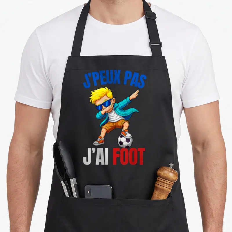 Tablier de cuisine noir avec illustration d'un garçon blond au dab posant sur un ballon de football sous le texte j'peux pas j'ai foot.