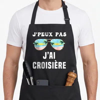 Tablier de cuisine noir avec lunettes de soleil reflétant une plage tropicale et le texte j'ai croisière