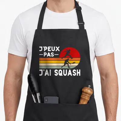 Tablier de cuisine noir avec motif j'peux pas j'ai squash et silhouettes de joueurs en style rétro.