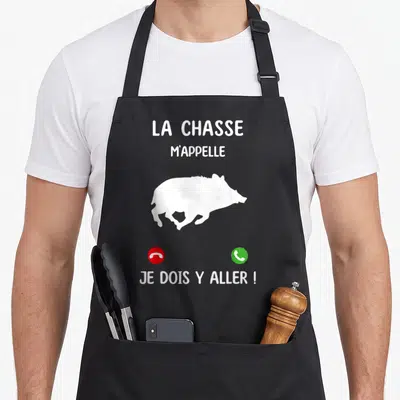 Tablier de cuisine noir avec silhouette de sanglier blanc et texte La chasse m'appelle Je dois y aller.
