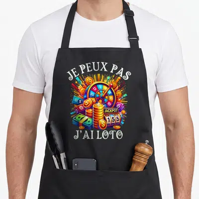 Tablier de cuisine noir avec une roulette multicolore, des piles de pièces dorées et le texte je peux pas j'ai loto.