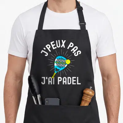 Tablier de cuisine noir avec une raquette de padel bleue, une balle jaune et le texte j'peux pas j'ai padel en blanc.