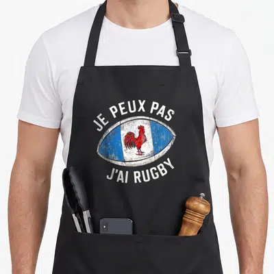 Tablier de cuisine noir avec un ballon ovale tricolore contenant un coq gaulois rouge et le texte je peux pas j'ai rugby en blanc.