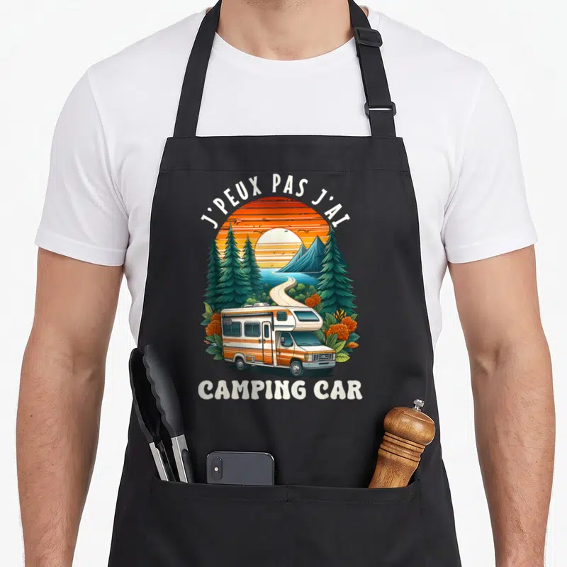 Tablier de cuisine noir avec illustration de camping-car au coucher du soleil entouré de pins et de fleurs orange.