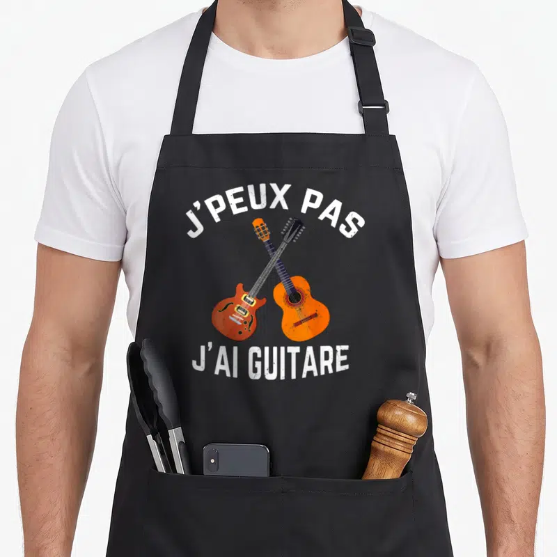 Tablier de cuisine noir avec deux guitares croisées orange et le texte blanc J'peux pas j'ai guitare.