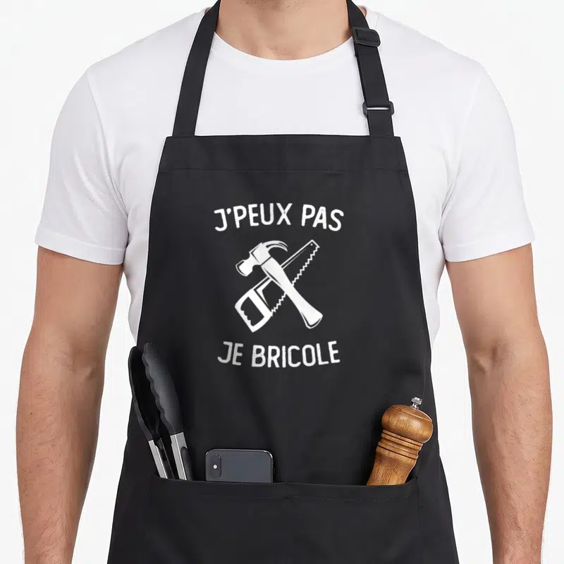 Tablier de cuisine noir avec marteau et scie croisés en blanc et texte j'peux pas je bricole