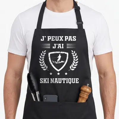 Tablier de cuisine noir avec inscription j'peux pas j'ai ski nautique et silhouette de skieur dans un écusson entouré de laurers.