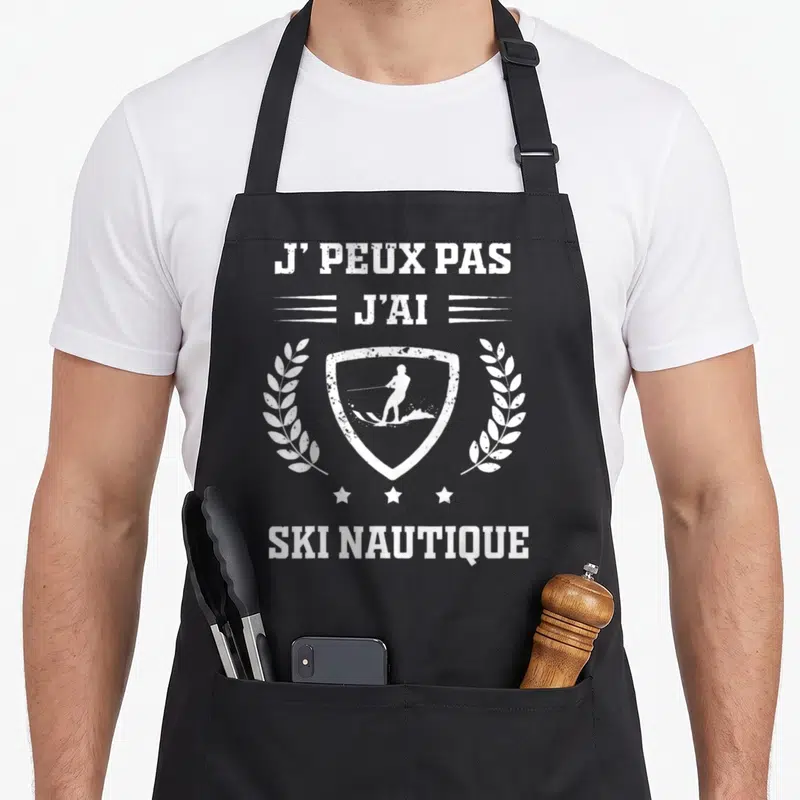 Tablier de cuisine noir avec inscription j'peux pas j'ai ski nautique et silhouette de skieur dans un écusson entouré de laurers.