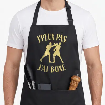 Tablier de cuisine noir avec inscription j'peux pas j'ai boxe et silhouettes de boxeurs dorées en action.