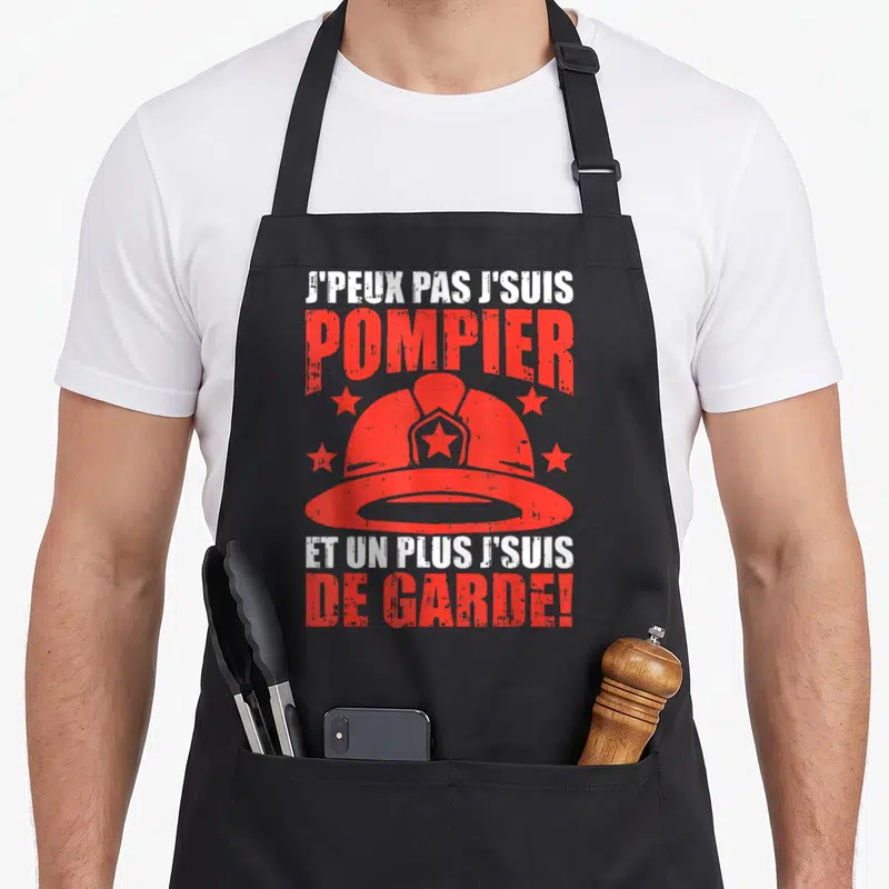 Tablier de cuisine noir avec casque de pompier rouge et texte blanc et orange.