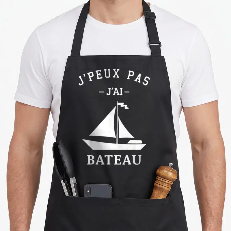 Tablier de cuisine noir avec illustration de voilier blanc et texte J'peux pas j'ai bateau.