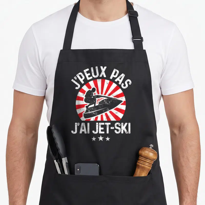 Tablier de cuisine noir avec motif j'peux pas j'ai jet-ski et silhouette de planche à moteur sur fond de rayons rouges.