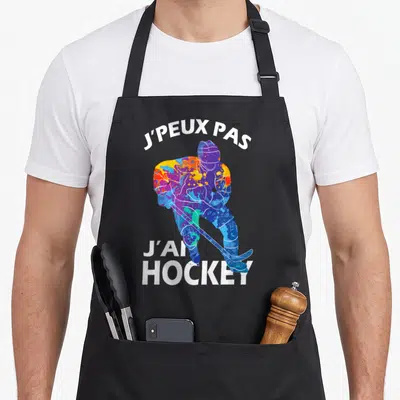 Tablier de cuisine noir avec joueur de hockey multicolore et texte j'peux pas j'ai hockey en blanc.