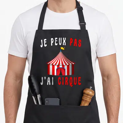 Tablier de cuisine noir avec une tente de cirque rouge et blanche et le texte je peux pas j'ai cirque imprimé en blanc et rouge.