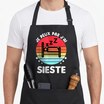 Tablier de cuisine noir avec motif rond coloré représentant un lit stylisé et des ZZZ au centre.