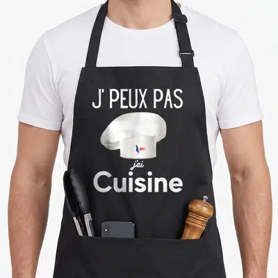 Tablier de cuisine noir avec une toque blanche portant un coq tricolore et le texte J'PEUX PAS J'AI CUISINE en blanc.