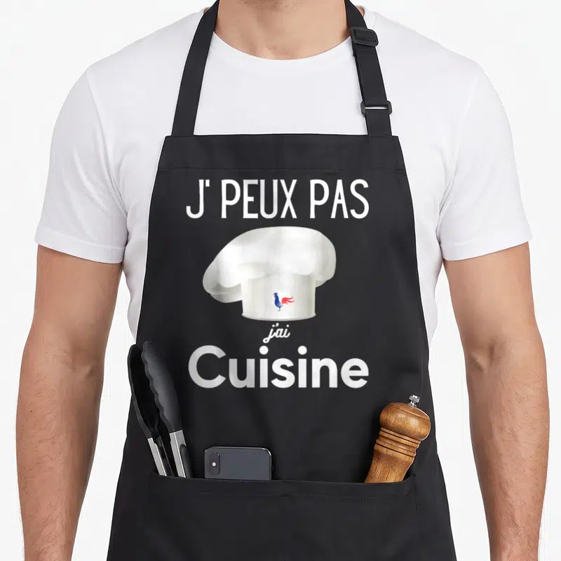 Tablier de cuisine noir avec une toque blanche portant un coq tricolore et le texte J'PEUX PAS J'AI CUISINE en blanc.