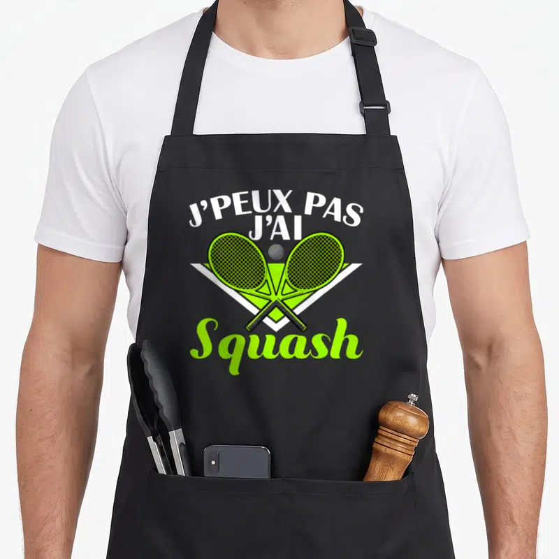 Tablier de cuisine noir avec deux raquettes de squash vertes croisées et le texte j'peux pas j'ai squash en blanc et vert fluo.