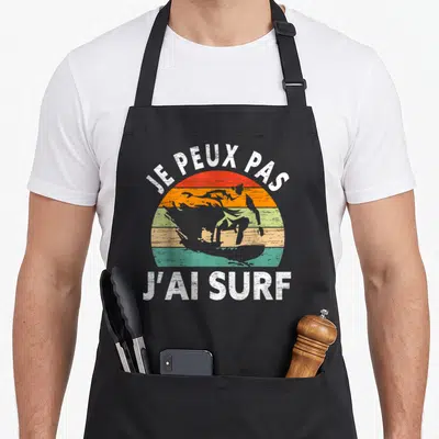 Tablier de cuisine noir avec planche de surf retro et texte je peux pas j'ai surf en blanc.