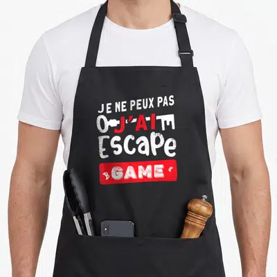 Tablier de cuisine noir avec le texte je ne peux pas j'ai un escape game en blanc et rouge.