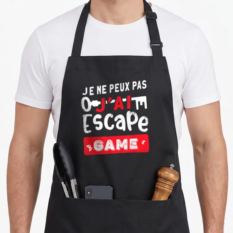 Tablier de cuisine noir avec le texte je ne peux pas j'ai un escape game en blanc et rouge.